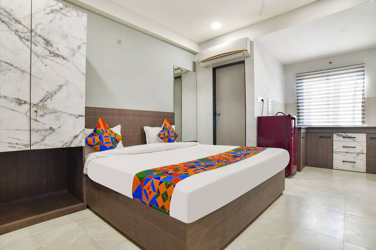A modern hotel room with a large bed, marble wall, and a small kitchenette.