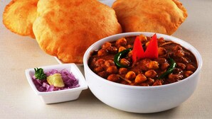 Een kom kikkererwten curry met gesneden uien en citroen, vergezeld van twee sneetjes brood.