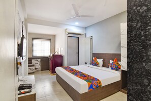 Habitación de hotel con cama, escritorio con computadora, armario, espejo y ventilador de techo.