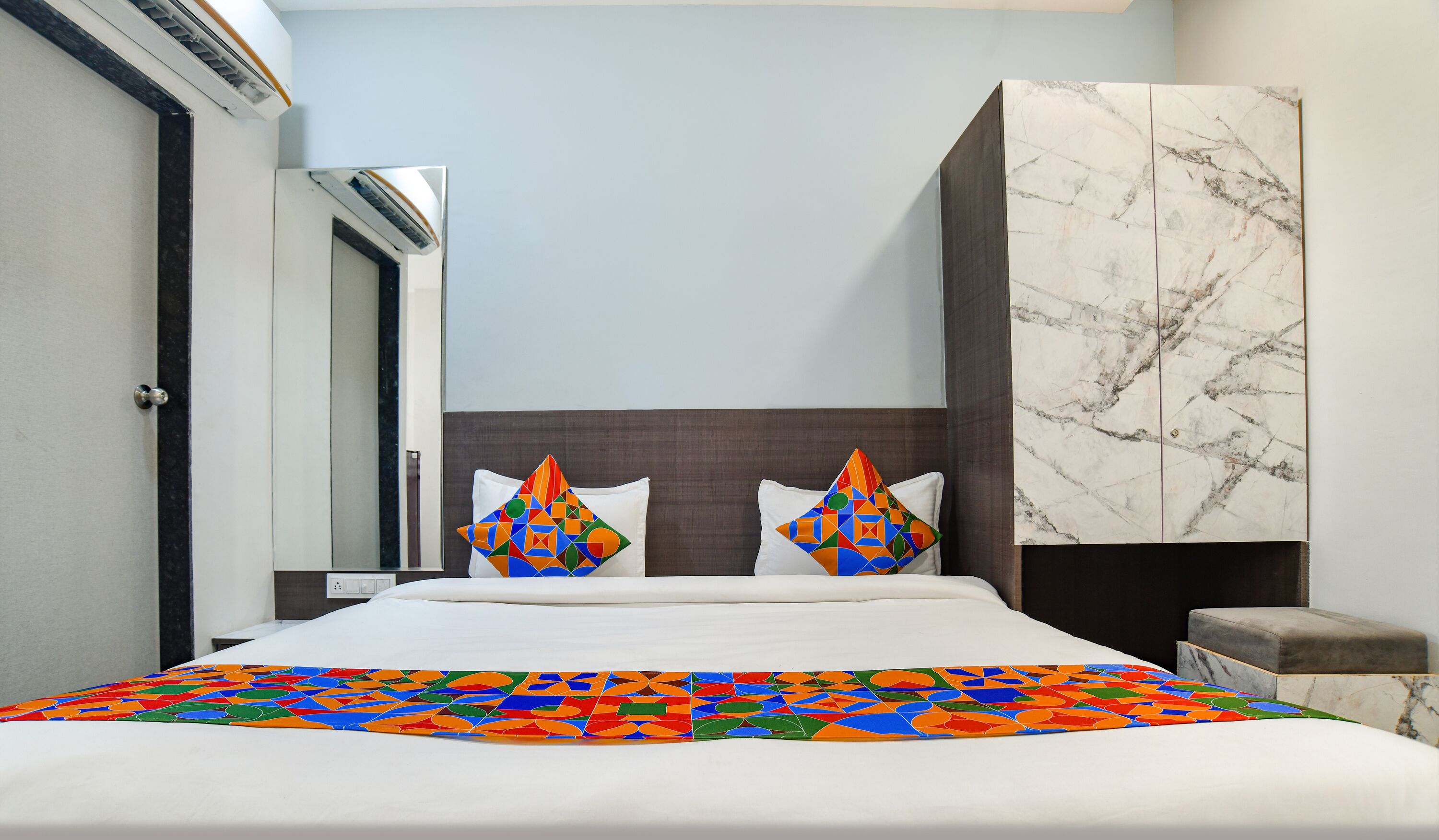 A hotel room with a bed, two pillows, a marble wall, and a wardrobe.