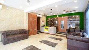 A hotel reception area with a reception desk, two sofas, a ceiling fan, and a stone wall. - FabHotel Dreamworld Residency (Barasat)