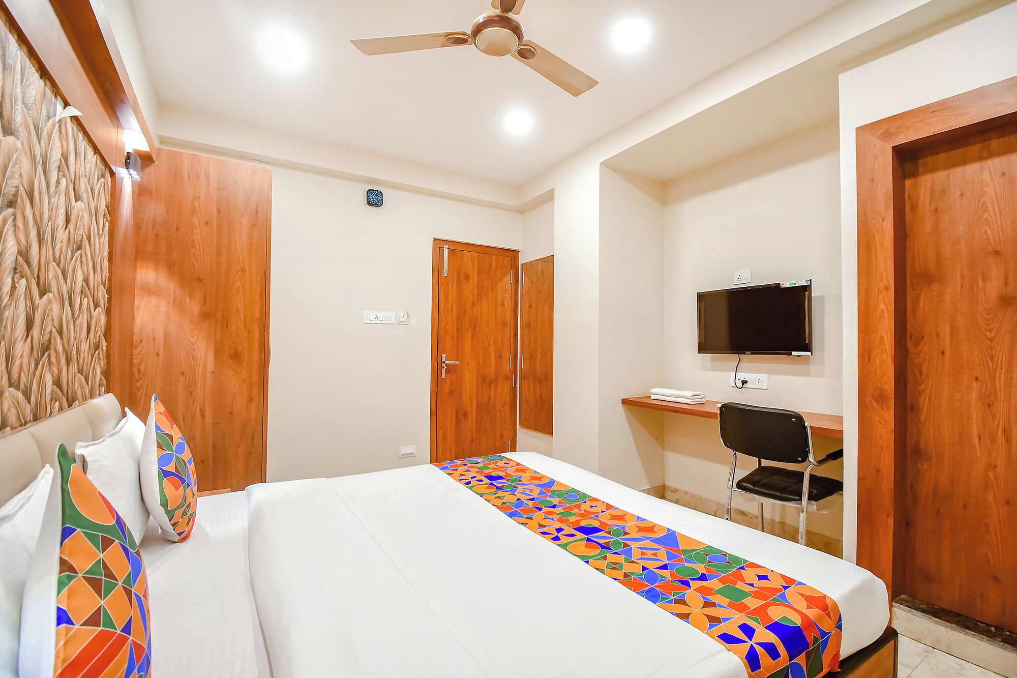 A hotel room with a bed, a desk with a chair, a television, and wooden doors.
