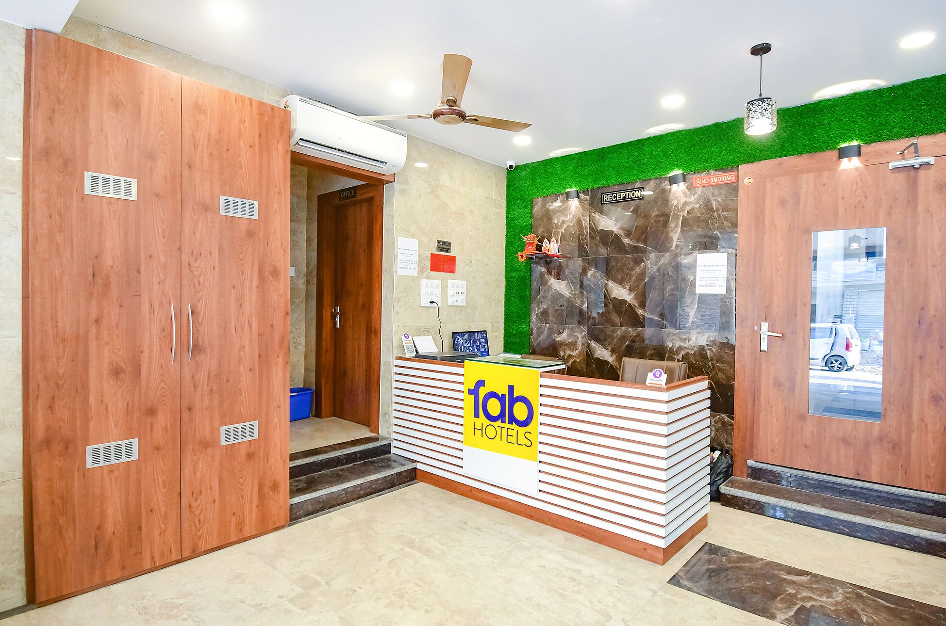 A hotel reception area with a wooden reception desk, a ceiling fan, and a green wall.