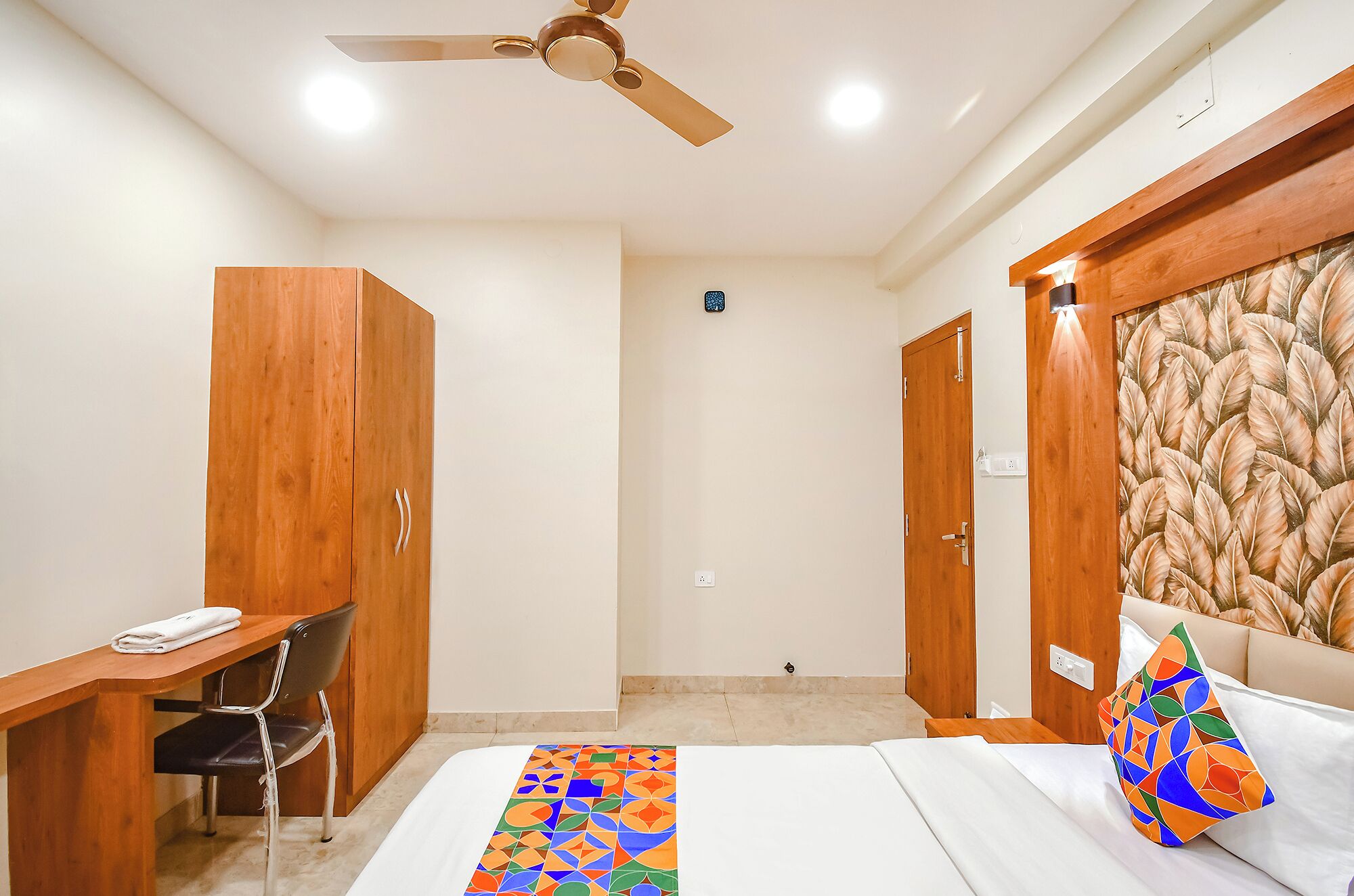 A hotel room with a bed, a desk, a chair, a wardrobe, and a ceiling fan.