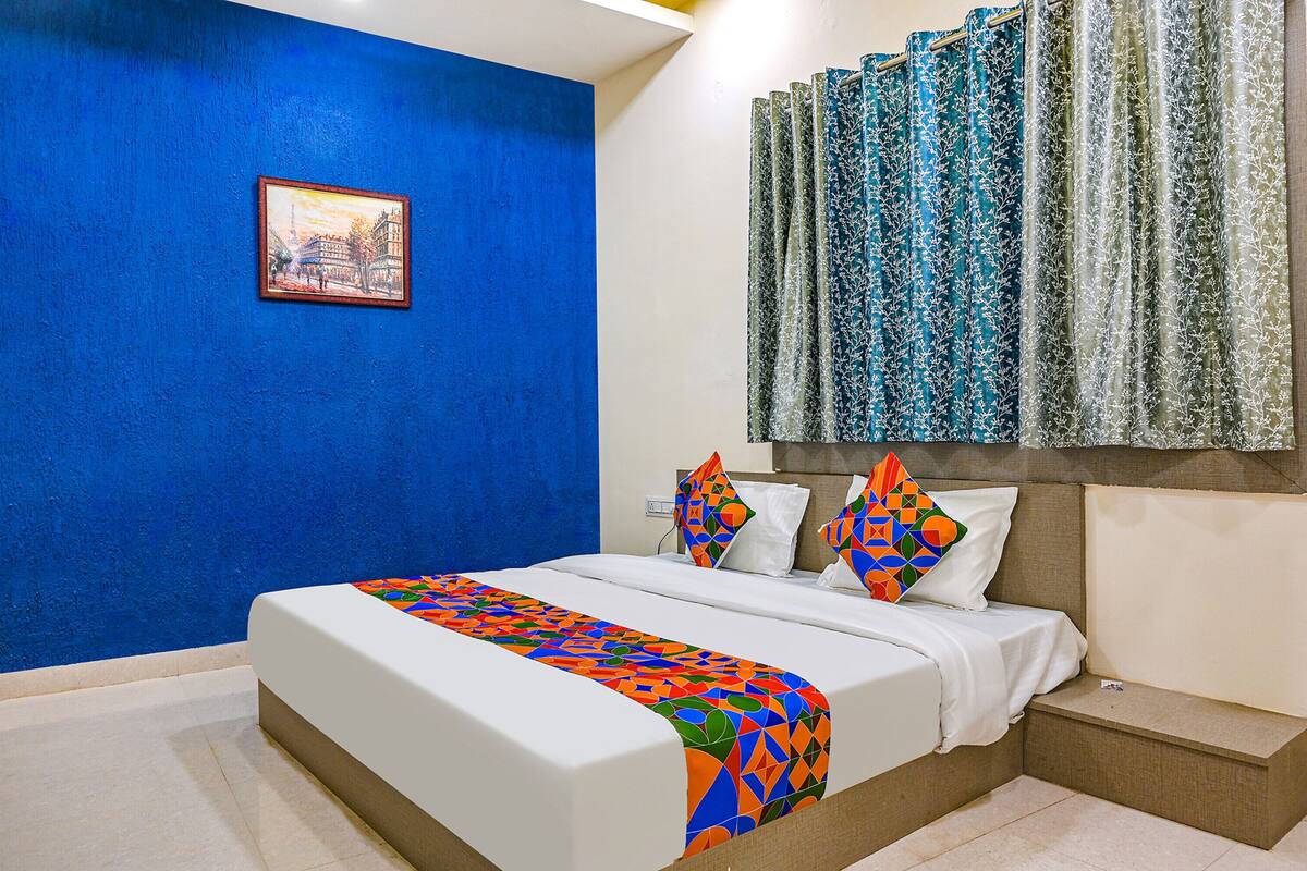 Habitación de hotel con una cama grande, una pared de acento azul, un cuadro y una cortina estampada.