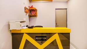 Un comptoir d’accueil avec une pancarte indiquant « RÉCEPTION », une imprimante et un petit autel où sont déposées des offrandes.