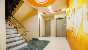 Un hall d’hôtel avec un escalier en marbre, une fresque murale jaune et un sol carrelé, propre et bien entretenu.