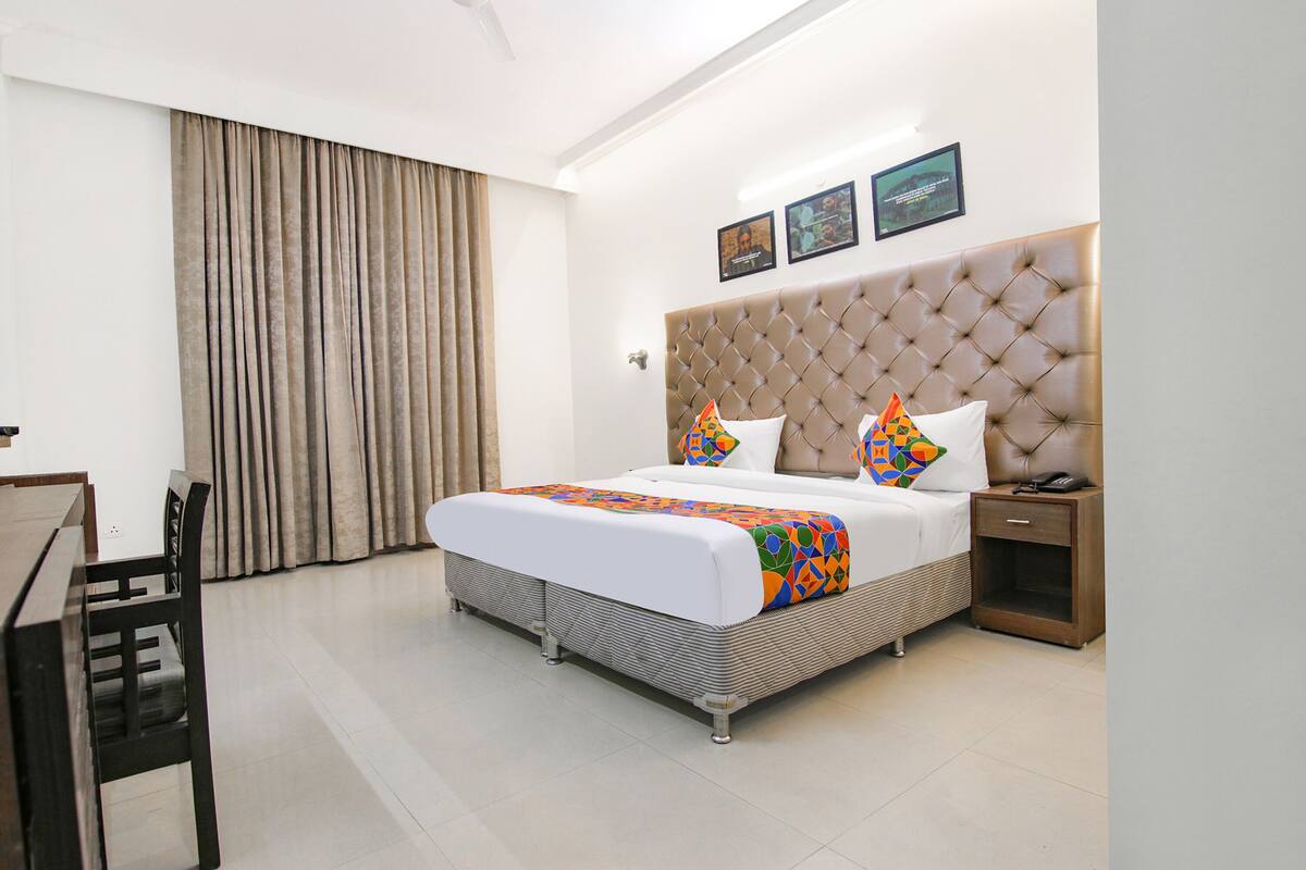 A modern hotel room with a large bed, a wooden nightstand, a desk, and a chair.