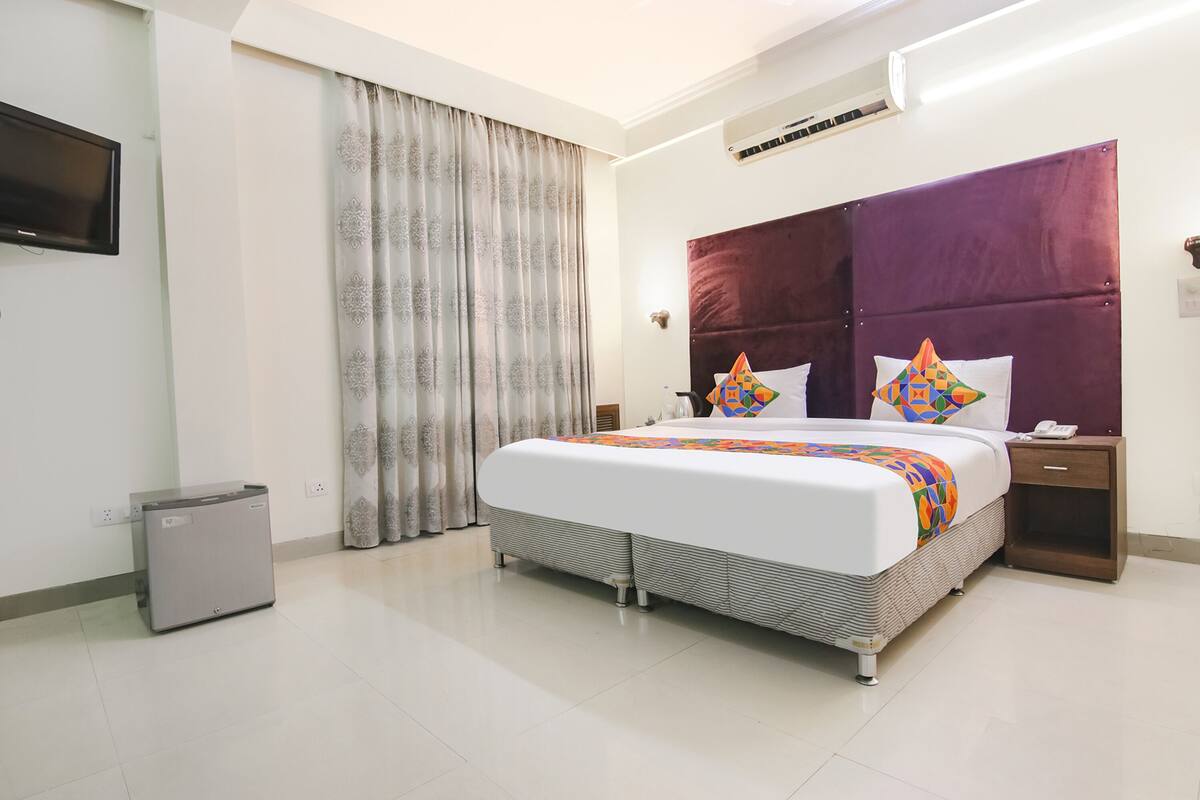 A hotel room with a bed, a TV, a small table, a nightstand, and a window with curtains.