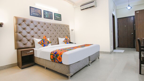 A bedroom with a tufted headboard, a bed with a colorful blanket, a bedside table, and a wooden wardrobe. - Fabhotel Rivlet Inn (Gurugram)