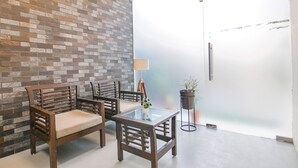A room with a brick wall, two wooden chairs, a glass table with a vase, a floor lamp, and a frosted glass door. - Fabhotel Rivlet Inn (Gurugram)