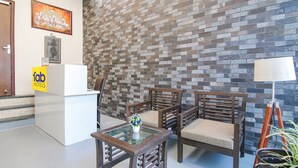 A reception area with a white desk, wooden chairs, a glass table with a vase, and a brick-patterned wall. - Fabhotel Rivlet Inn (Gurugram)