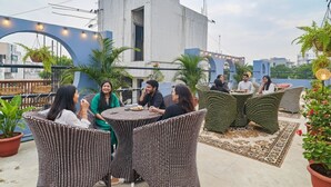 A rooftop terrace with wicker furniture, potted plants, and string lights.