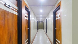 A hallway with wooden doors, each marked with a number. The floor is tiled, and the hallway is well-lit with ceiling lights.