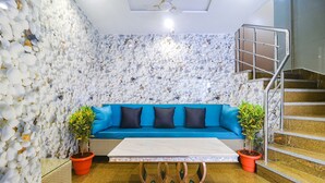 A modern interior with a white stone wall, a blue sofa with black cushions, a white coffee table, and a staircase with metal railings.