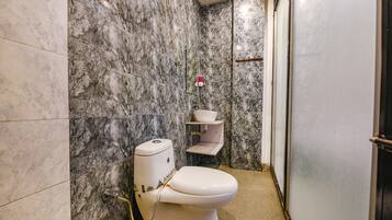 A bathroom with a toilet, marble walls, and a small shelf with a bowl.