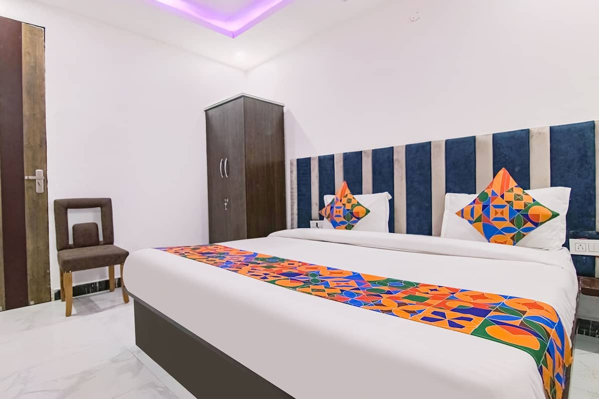 A hotel room with a bed, a wardrobe, a chair, and a headboard with decorative pillows.