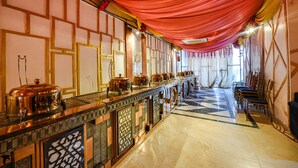 A long buffet table with food service equipment, a checkered floor, and a row of chairs on the right. - Fabhotel The Dreams (Kharar)