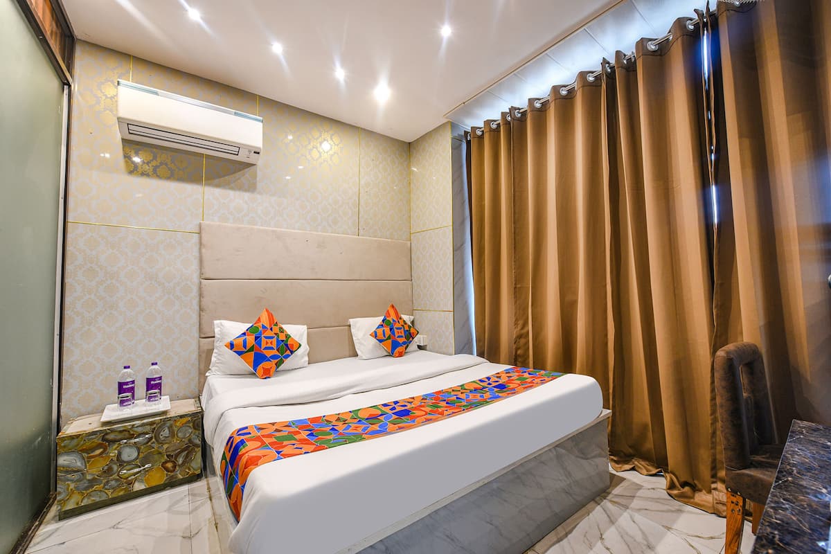 A hotel room with a bed, a headboard, a nightstand with toiletries, a chair, and a curtain.
