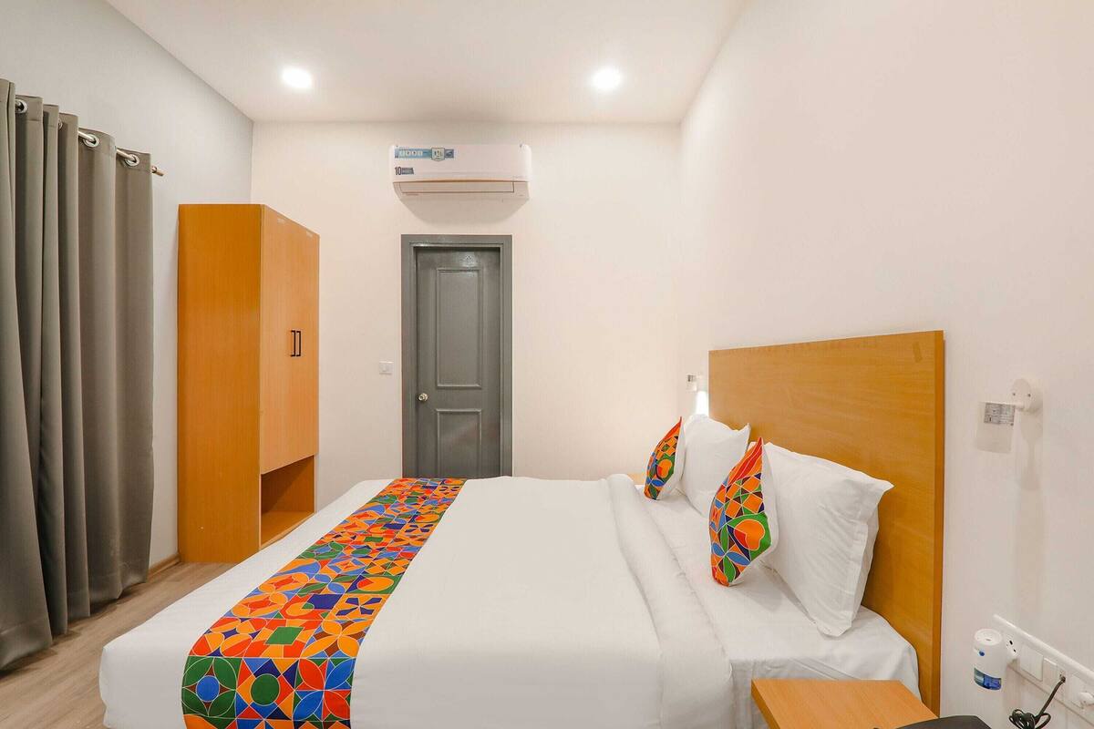 Una habitación de hotel con una cama, un armario, un aire acondicionado, una puerta y una mesita de noche.