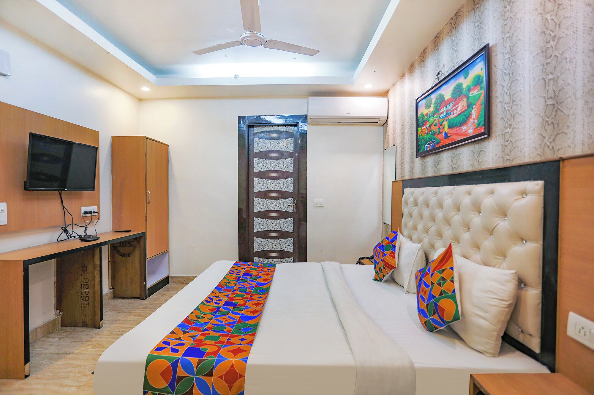 A hotel room with a bed, a desk, a television, and a ceiling fan.