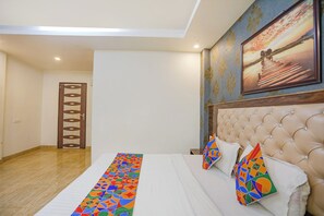 A hotel room with a bed, a headboard, a painting, and a door with a geometric pattern. - FabHotel Joystick (Noida)