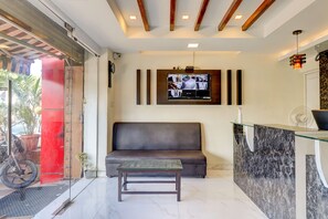 Un área de recepción con un sofá, una mesa de vidrio, un televisor montado en la pared y techo de madera.