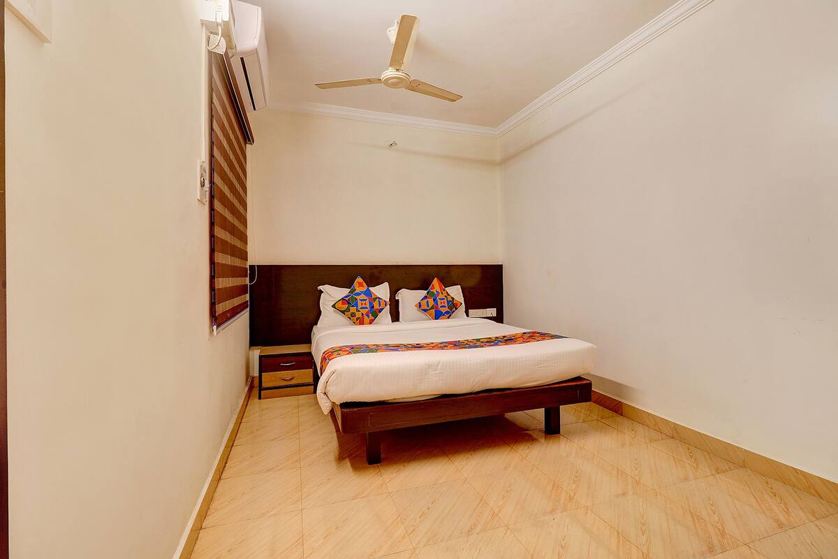 Un dormitorio con cama, mesita de noche, cabecera de madera, ventilador de techo y ventana con persianas.