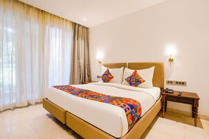 Habitación de hotel con una cama grande, dos lámparas de noche, una mesita de noche con un teléfono y una ventana con cortinas traslúcidas.