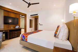 Una habitación de hotel con una cama, televisión, escritorio y ventilador de techo.