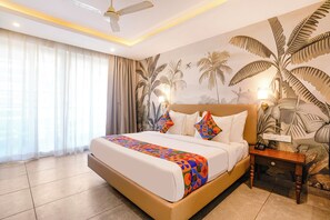 A hotel room with a bed, curtains, a ceiling fan, a nightstand, and a wall mural. - FabHotel Prime The King's Court - 700M From Calangute Beach (Calangute)