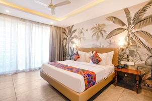 A hotel room with a bed, curtains, a ceiling fan, a nightstand, and a wall mural.