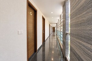 A corridor with wooden doors, a marble wall, and a glass railing.