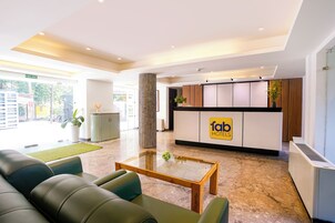 A hotel reception area with a reception desk, a fire exit sign, a reception counter, a coffee table, and a seating area with sofas.