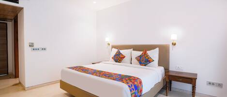 A hotel room with a bed, bedside table, nightstand, wall-mounted lamp, and a ceiling fan.