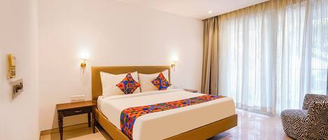 A hotel room with a large bed, a ceiling fan, a nightstand, a chair, and a window with curtains.