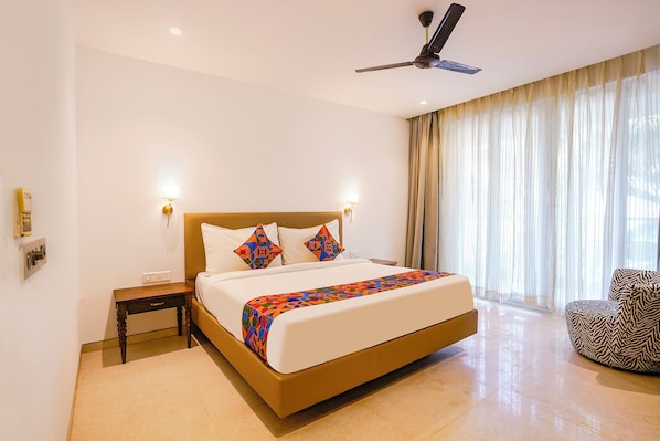 A hotel room with a large bed, a ceiling fan, a nightstand, a chair, and a window with curtains.