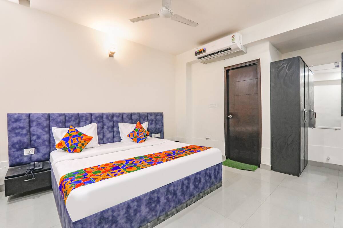 A bedroom with a bed, a nightstand, a wardrobe, a door, and an air conditioning unit.