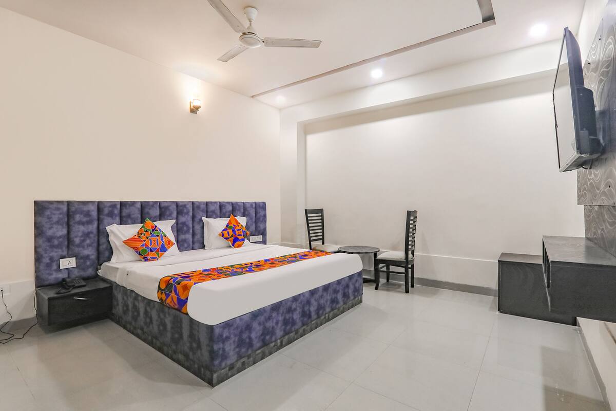 A modern hotel room with a large bed, a ceiling fan, a flat-screen TV, and a small seating area.