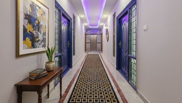 A hallway with blue doors, a patterned carpet, and a potted plant on a wooden table. - Fabhotel E City Inn (Bengaluru)