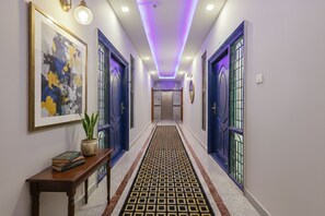 A hallway with blue doors, a patterned carpet, and a potted plant on a wooden table. - FabHotel E City Inn - 3 Km from Infosys Campus (Bengaluru)