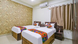 A hotel room with two beds, a wooden headboard, a nightstand with a bottle, and an air conditioning unit on the wall. - Fabhotel E City Inn (Bengaluru)