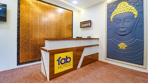 A reception desk with a logo, a Buddha statue, and a textured wall. - Fabhotel E City Inn (Bengaluru)