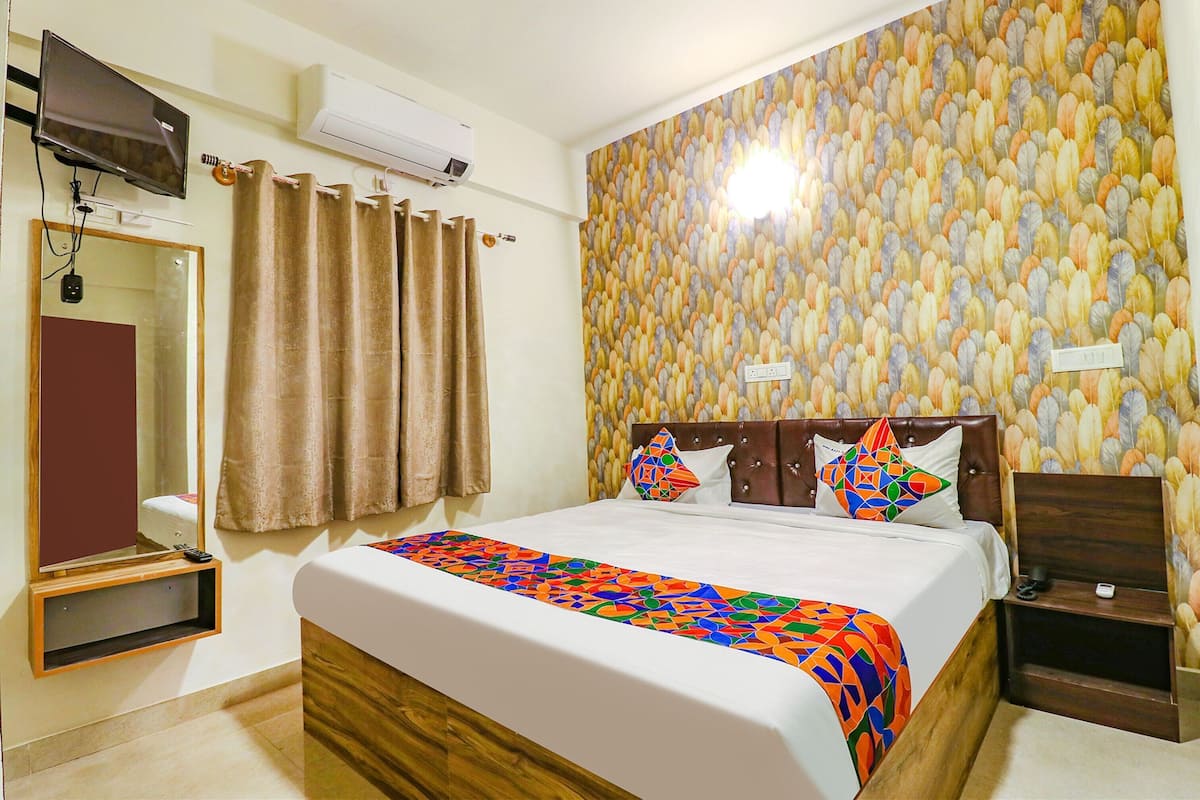 A hotel room with a bed, a TV, a mirror, a curtain, and a wall with a feather pattern.