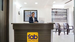 A hotel reception desk with a logo, a receptionist, a laptop, and a seating area with chairs. - FabHotel Destination 42 (Pune)