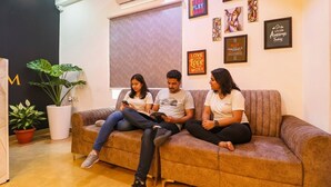 Three people sitting on a sofa in a room with a large window, a potted plant, and several framed motivational quotes on the wall. - FabExpress The Dream Elite (Hyderabad)