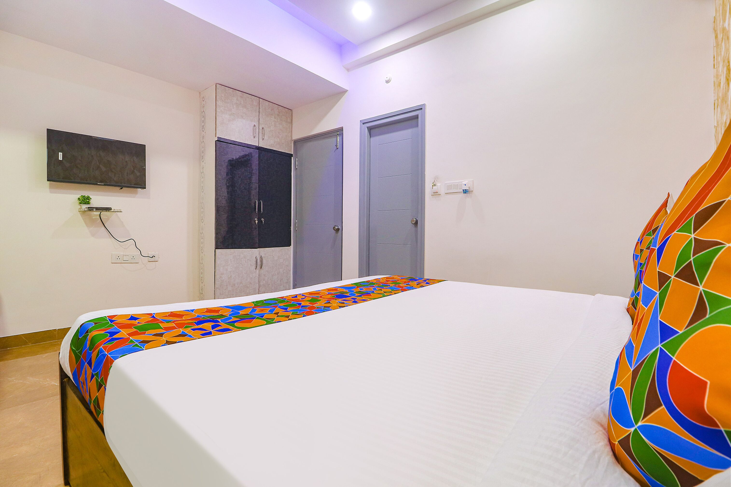 A bedroom with a bed, a TV mounted on the wall, and two doors.
