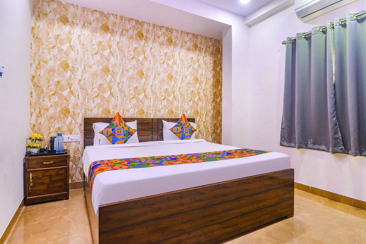A bedroom with a wooden bed, patterned wallpaper, a nightstand, and a window with curtains.