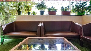 A brown leather sofa and a glass-top coffee table in a room with a green carpet and potted plants on a raised platform. - FabHotel White Gold (Navi Mumbai)