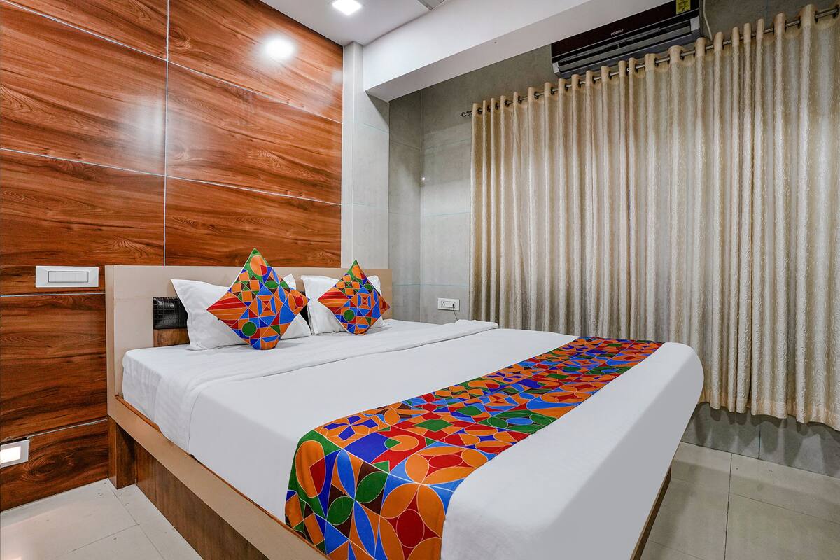 Une chambre d’hôtel moderne avec un mur d’accent en bois, un grand lit avec une literie aux couleurs vives et une grande fenêtre avec des rideaux.